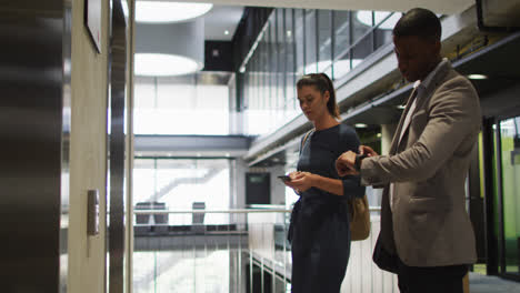 Diverse-businessman-and-businesswoman-waiting-for-lift-and-arriving-in-modern-office