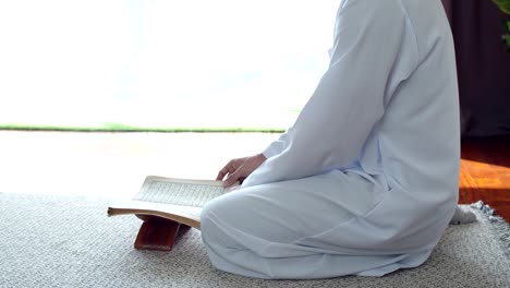 young muslim man wearing islamic clothes reading the quran