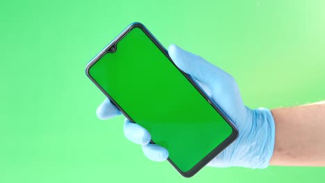 person in blue glove holding a smartphone with a green screen