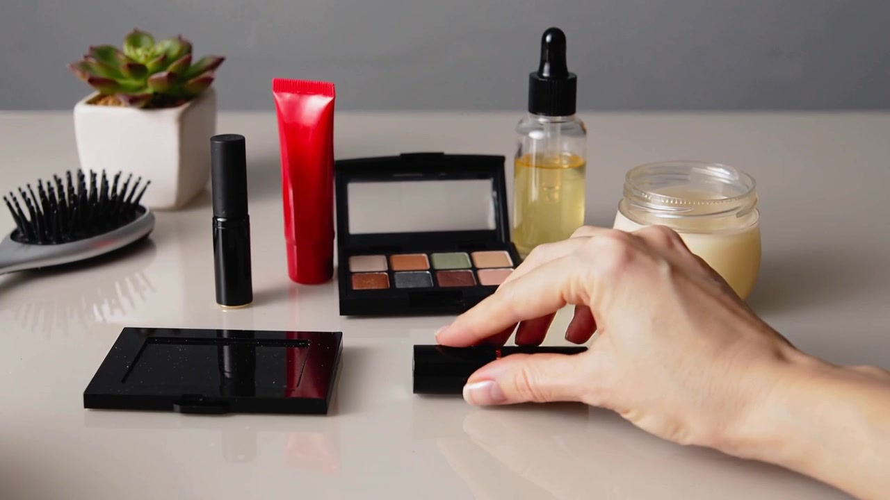 Reaching hands arranging and checking makeup on tabletop, preparing display with red tube, palette