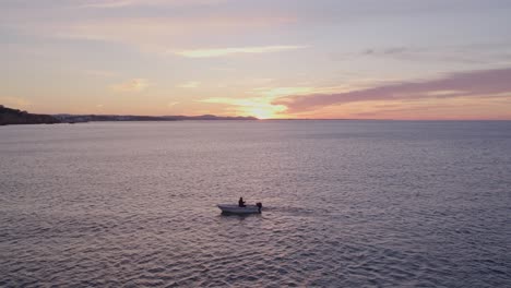 Man-is-fishing-in-small-boat-on-calm-sea-during-sunrise,-aerial