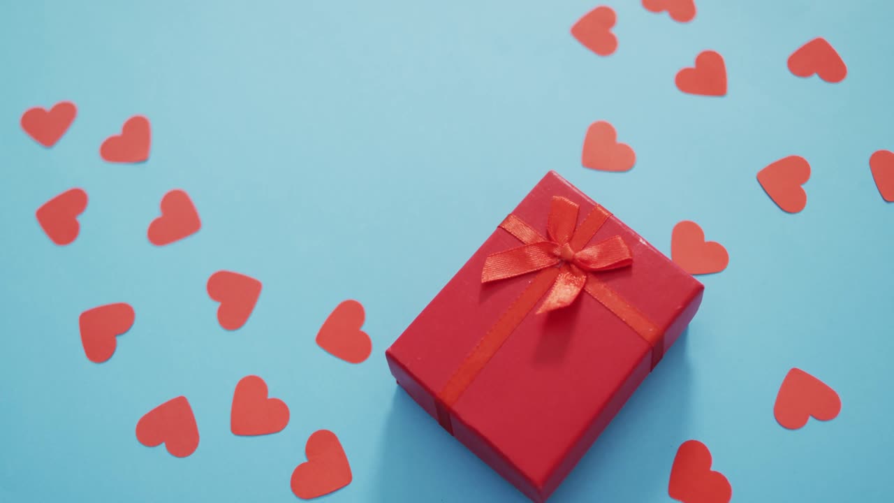 Multiple red paper hearts and red present at valentine's day on blue background