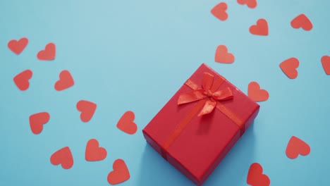 Multiple-red-paper-hearts-and-red-present-at-valentine's-day-on-blue-background