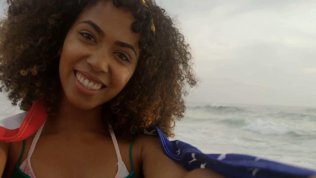 Tampak depan wanita Afrika-Amerika terbungkus bendera Amerika berdiri di pantai 4k