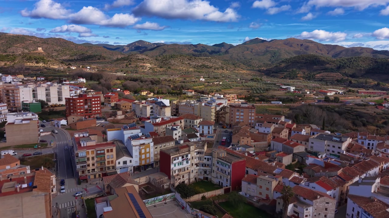 Chelva, pueblo tradicional español enclavado entre montañas verdes en la región de Valencia, con tejados de terracota, fachadas coloridas y cielo azul nublado
