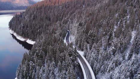 aerial cinematic view of car drive on a forest road in winter with snow on top