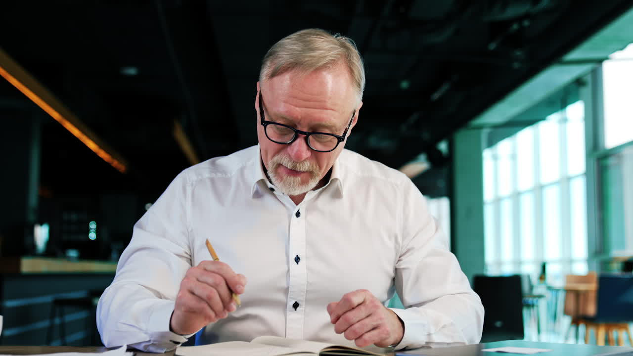 Positive Caucasian businessman in white shirt and glasses in office. Man looks at his notes and opens the laptop. Close up.