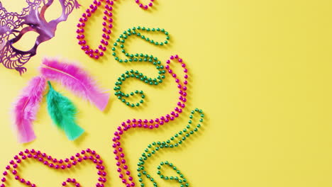 video of pink mask, mardi gras carnival beads and feathers on yellow background with copy space