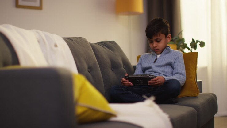 Giovane ragazzo seduto sul divano a casa che gioca o guarda contenuti in streaming su un dispositivo di gioco portatile 6