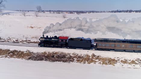 vista aérea de una antigua locomotora de vapor que se acerca tirando de automóviles de pasajeros y soplando humo y vapor después de una tormenta de nieve