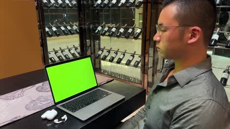 hombre millennial asiático rico mirando una computadora portátil con pantalla verde en una casa de lujo con pared de vino