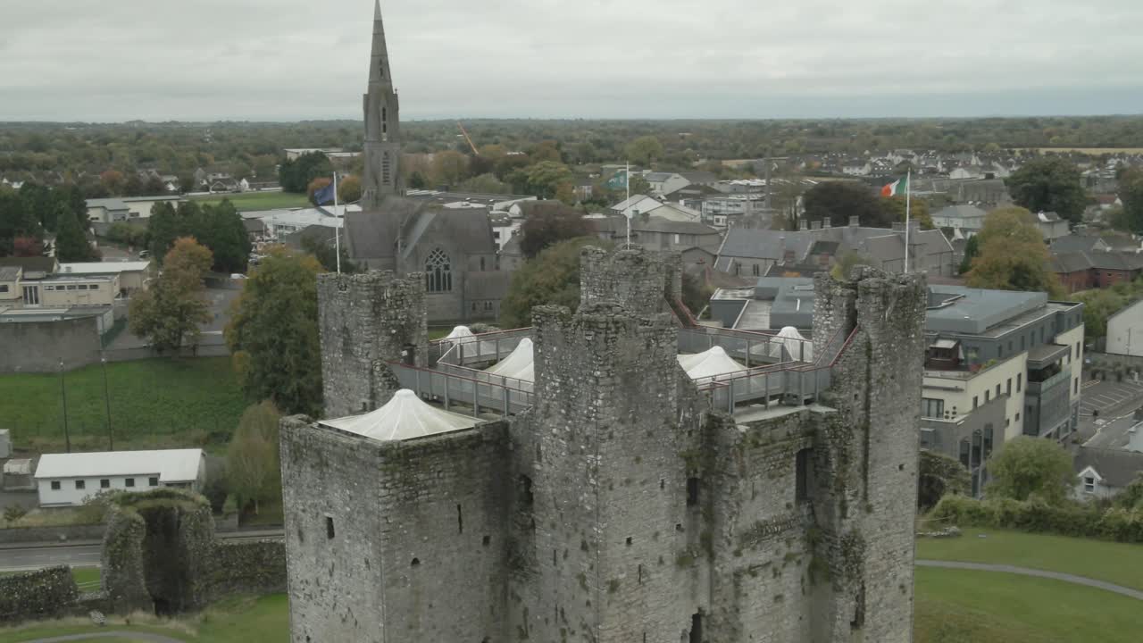 Flags On The Tower Of Trim Castle With St. Patricks Church In The Distance In County Meath, Ireland. - aeriala shot