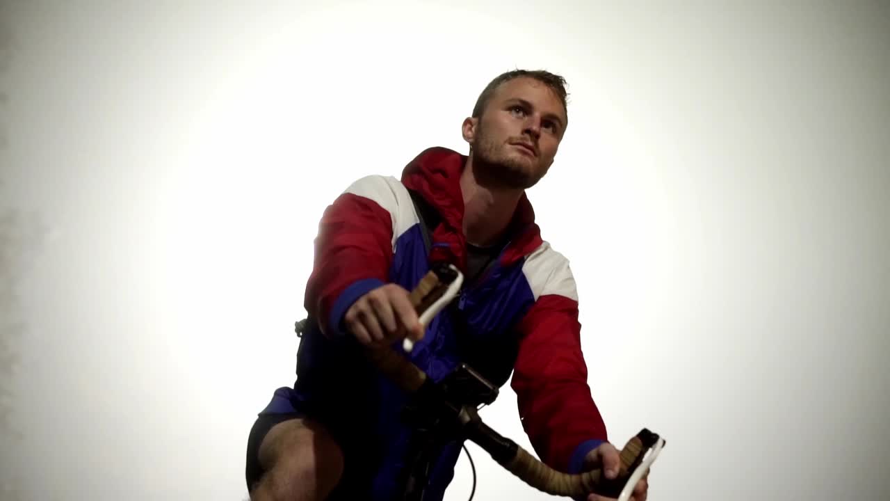 hombre atlético listo para despegar en bicicleta, retroiluminado por la luz de la calle en una noche nublada en cámara lenta