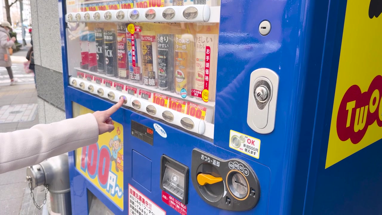 Uma mão insere moedas e pressiona botões em uma máquina de venda automática azul em Tóquio, Japão.