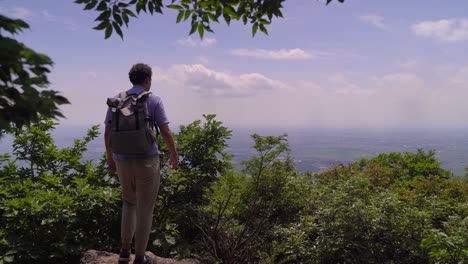 male hiker enjoying the beautiful views from top of lush mountain - medium shot