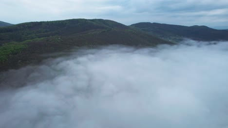 lower tatras mountains aerial view with dense low mist clouds or fogs covering the valley on cloudy morning in slovakia, banska bystrica