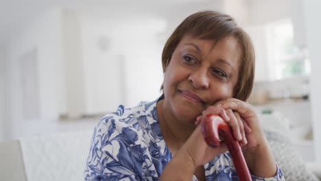 Happy-african-american-senior-woman-sitting-leaning-on-walking-stick,-looking-away-smiling