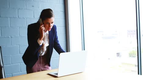 Businesswoman-talking-on-mobile-phone-while-using-laptop