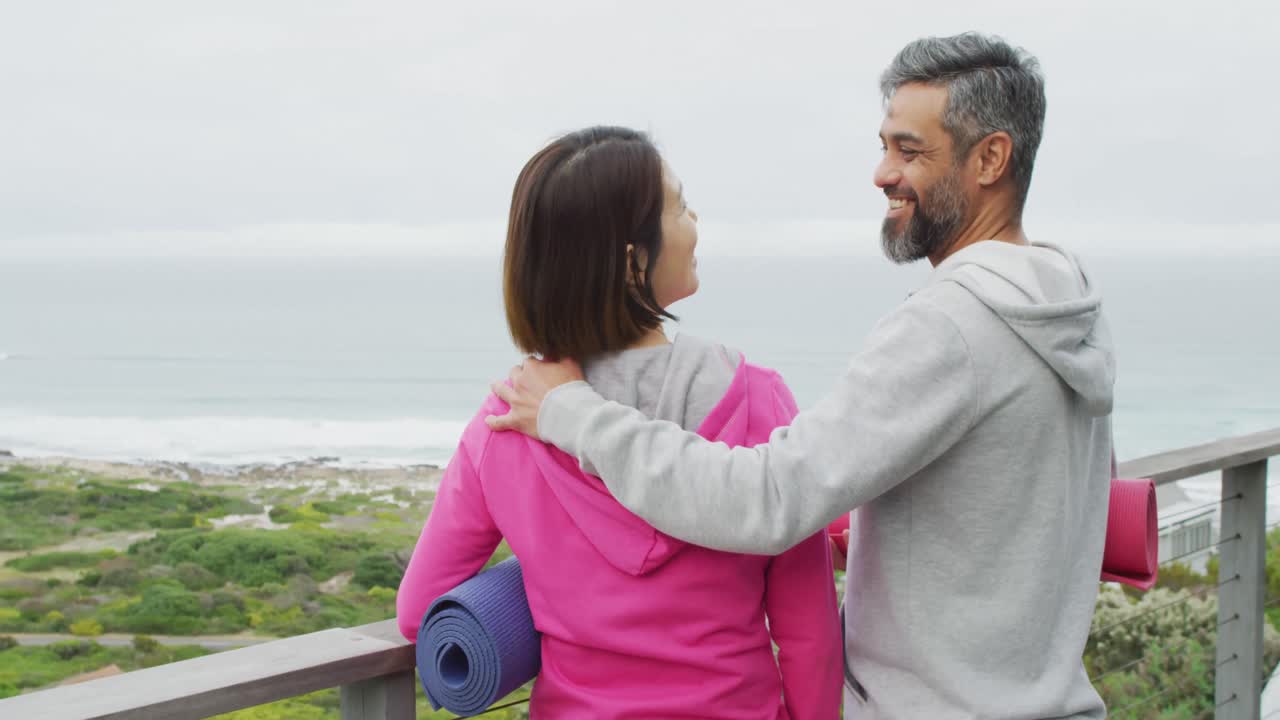 다양한 행복한 커플이 요가 매트를 들고 발코니에서 포옹하고 있습니다.