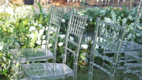 transparent chairs arranged for outdoor wedding ceremony with white flowers, elegant event setup