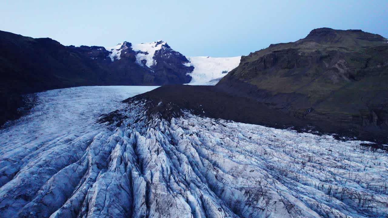 Aerial: A Glacier's serpentine path with deep crevasses and jagged ice formations, evidence of the climate change impact on the constant movement and transformation of this natural wonder