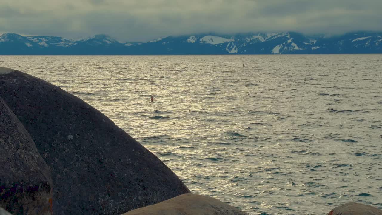 구름으로 둘러싸인 배경에 눈 덮인 산이 있는 사우스 레이크 타호 측면에 있는 큰 바위 암석 - 모래 항구