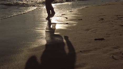 ombre d'un jeune garçon insouciant au ralenti qui traverse la plage de sable doré et humide au lever du soleil