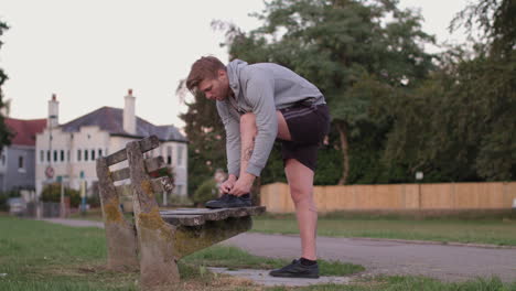 young athletic man ties his shoes on bench in park before he sets off on run