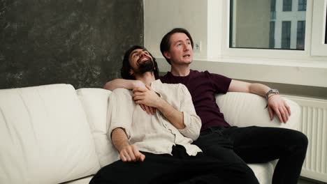 Two-men-couple-relaxing-on-the-couch,-happy-about-new-house