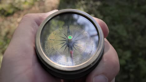 traveler hand holds a old directional compass in summer forest. person use compass to find location. travel concept close-up.