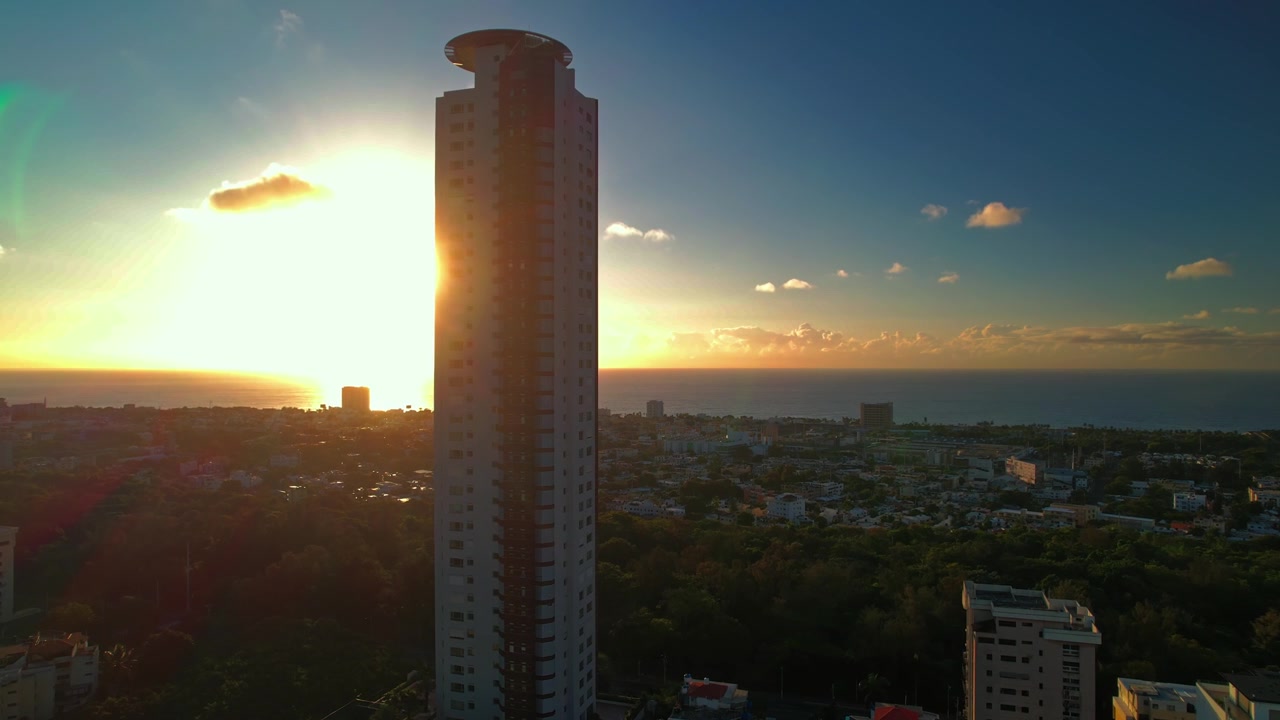 Tomada aérea de drone em ângulo alto movendo-se para a esquerda e descendo atrás da icônica Torre Caney, criando um efeito de reflexo solar sobre a costa do mar do Caribe durante o pôr do sol