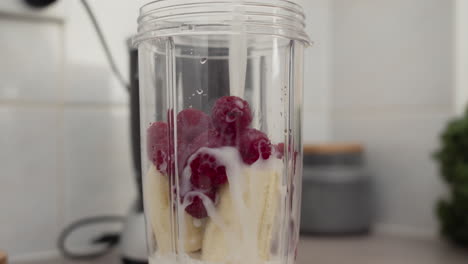 pouring milk into raspberries and banana mix to make vitamin smoothie