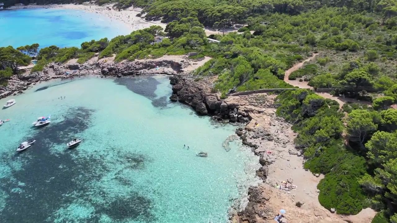 Goditi viste mozzafiato della spiaggia di Cala Agulla a Cala Rajada, Maiorca, che mostra acque cristalline, coste sabbiose e barche che navigano nelle vicinanze. Vivi la bellezza di questo luogo sereno.