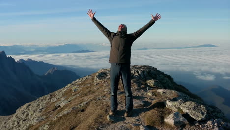 man celebrating on a mountain peak above the clouds