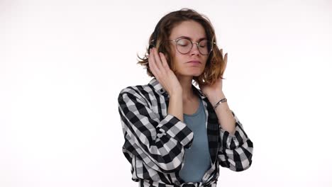chica joven atractiva en camisa a cuadros bailando y cantando con grandes auriculares música y sentirse bien concepto aislado en fondo de estudio blanco