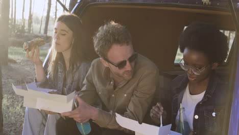 a multiethnic group of friends eating in the back of a caravan in the middle of the forest