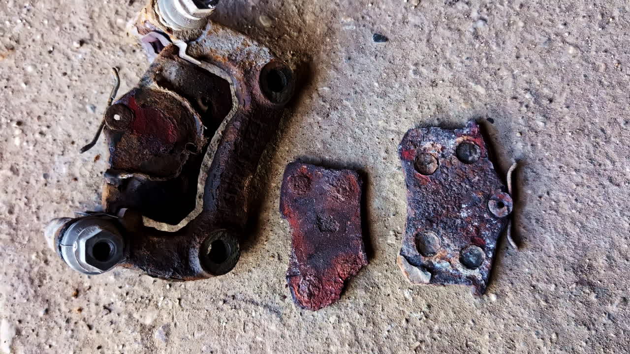 Severely rusted and disintegrated brake caliper and pads on ground