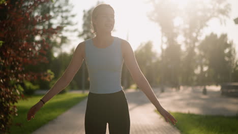 young lady smiling while skating outdoors, swinging her hands for balance, with sunlight reflecting off her creating a bright glow, blurred background featuring lush greenery and trees