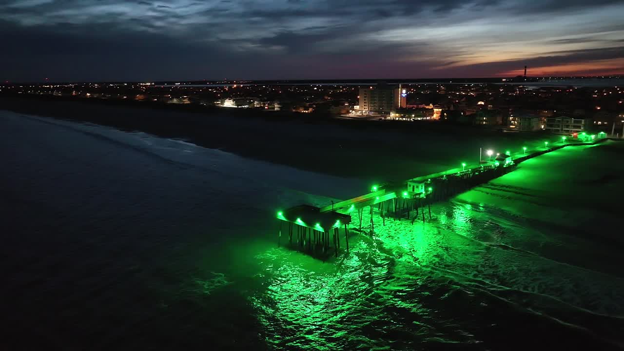 Cinematic aerial view of pier in late evening, illuminated with green light