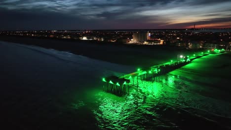 Filmische-Luftaufnahme-Des-Piers-Am-Späten-Abend,-Mit-Grünem-Licht-Beleuchtet