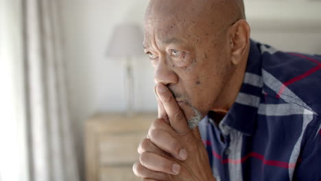 Thoughtful-senior-biracial-man-looking-through-window-in-bedroom,-slow-motion