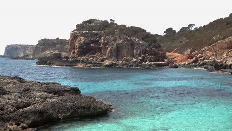 wide shot of rocky coastline and cliffs with turquoise colored water at caló des moro bay on mallorca island