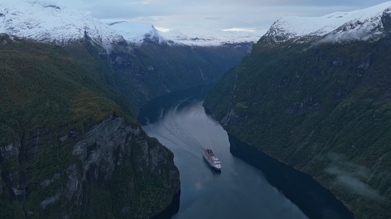 Vista con drone di una nave che naviga il Geirangerfjord con montagne innevate