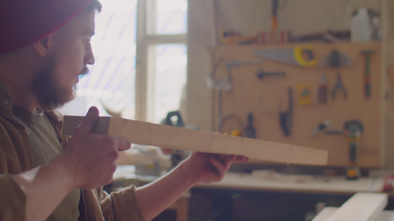 Carpenter Blowing Dust from Wooden Plank
