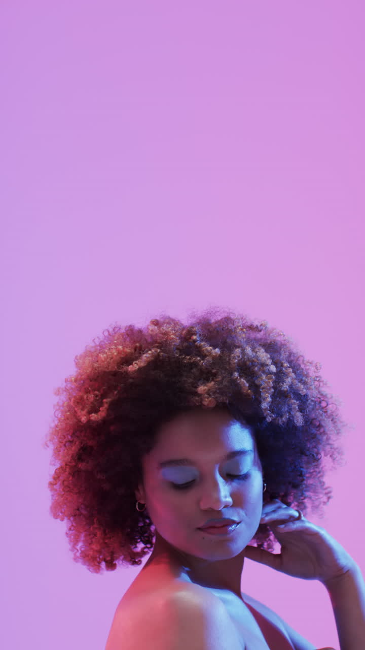 Vertical video of biracial woman with dark hair in blue and pink light with copy space, slow motion