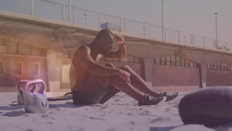 Manchas-De-Luz-Contra-Un-Hombre-Afroamericano-Cansado-Tomando-Un-Descanso-De-Hacer-Ejercicio-En-La-Playa