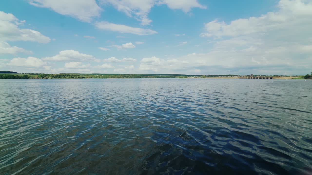 View from the side deck of the yacht. Motor boat moves along the shore, creating waves.