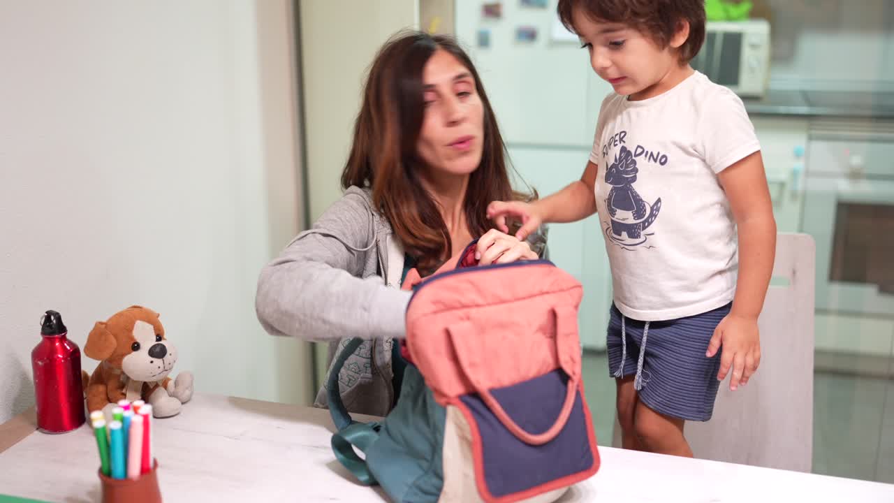 A mother helps her child pack his backpack
