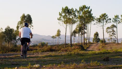 a cyclist rides on a dirt path surrounded by scenic pine trees under a clear sky. the dynamic scene captures the essence of outdoor exploration.