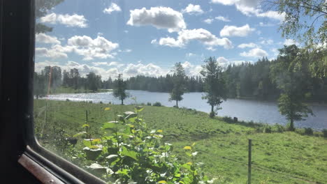 Looking-through-the-windows-of-an-old-orange-train---railcar-that-are-moving,-outside-a-lake-is-passing-by